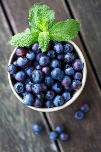 This is a bunch of fresh blueberries in a handmade ceramic bowl. The focus is on the blueberry in the center and falls off quickly.